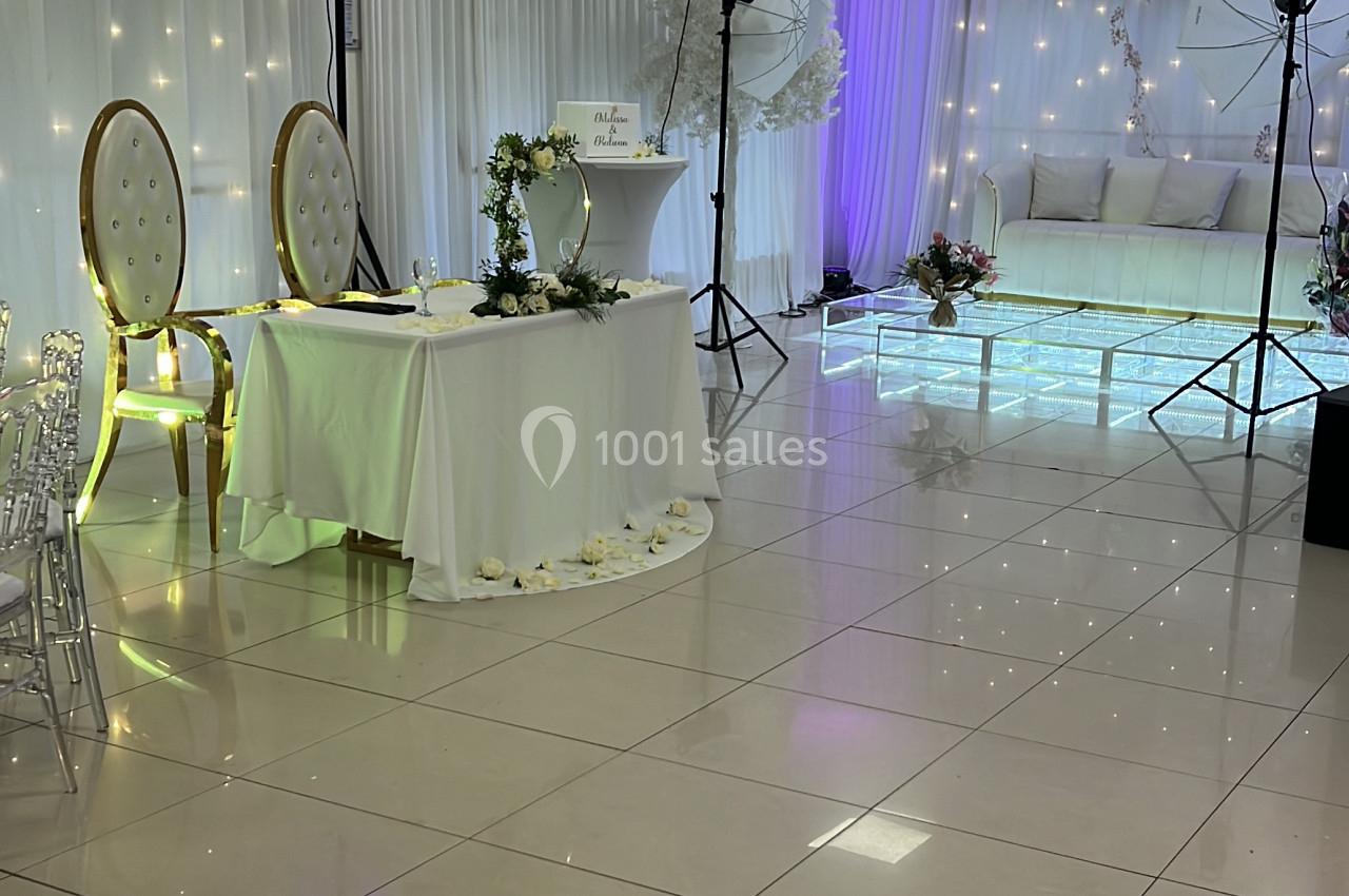 Salle de réception décorée avec des chaises dorées, une table blanche, des lumières suspendues et un éclairage coloré.