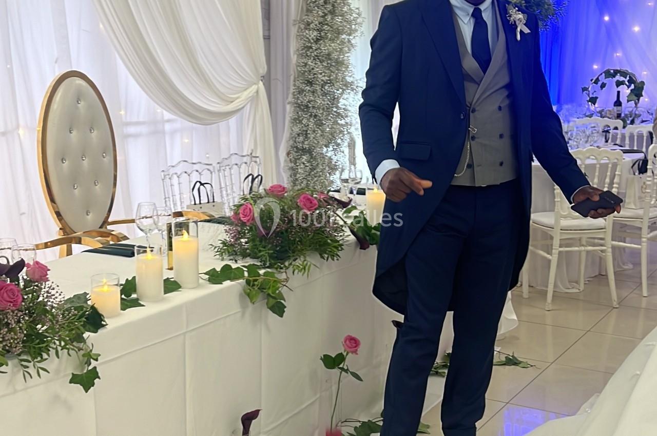 Un homme en costume sombre se tient debout dans une salle décorée pour un mariage avec fleurs et bougies.