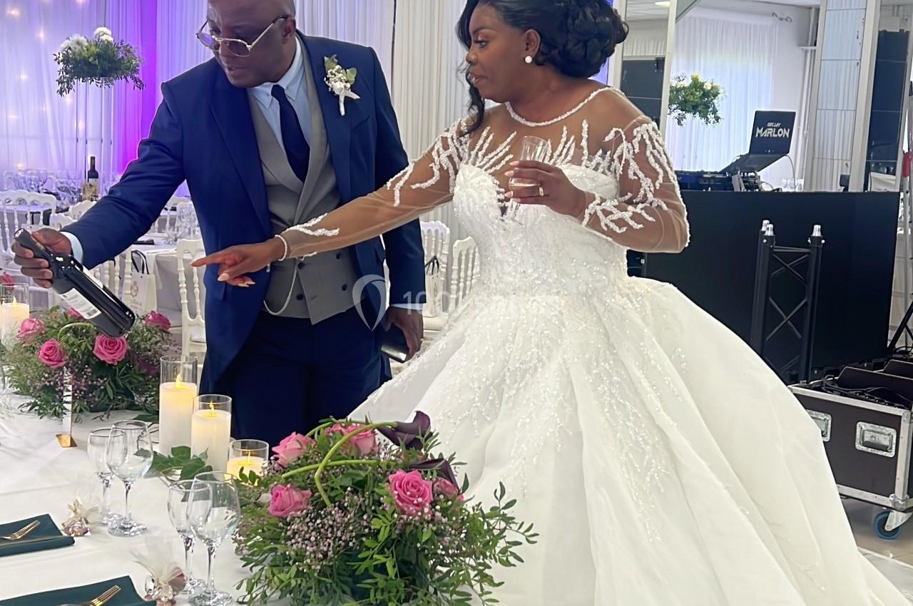 Un couple en tenue de mariage ajuste une table décorée de fleurs et de bougies dans une salle de réception.