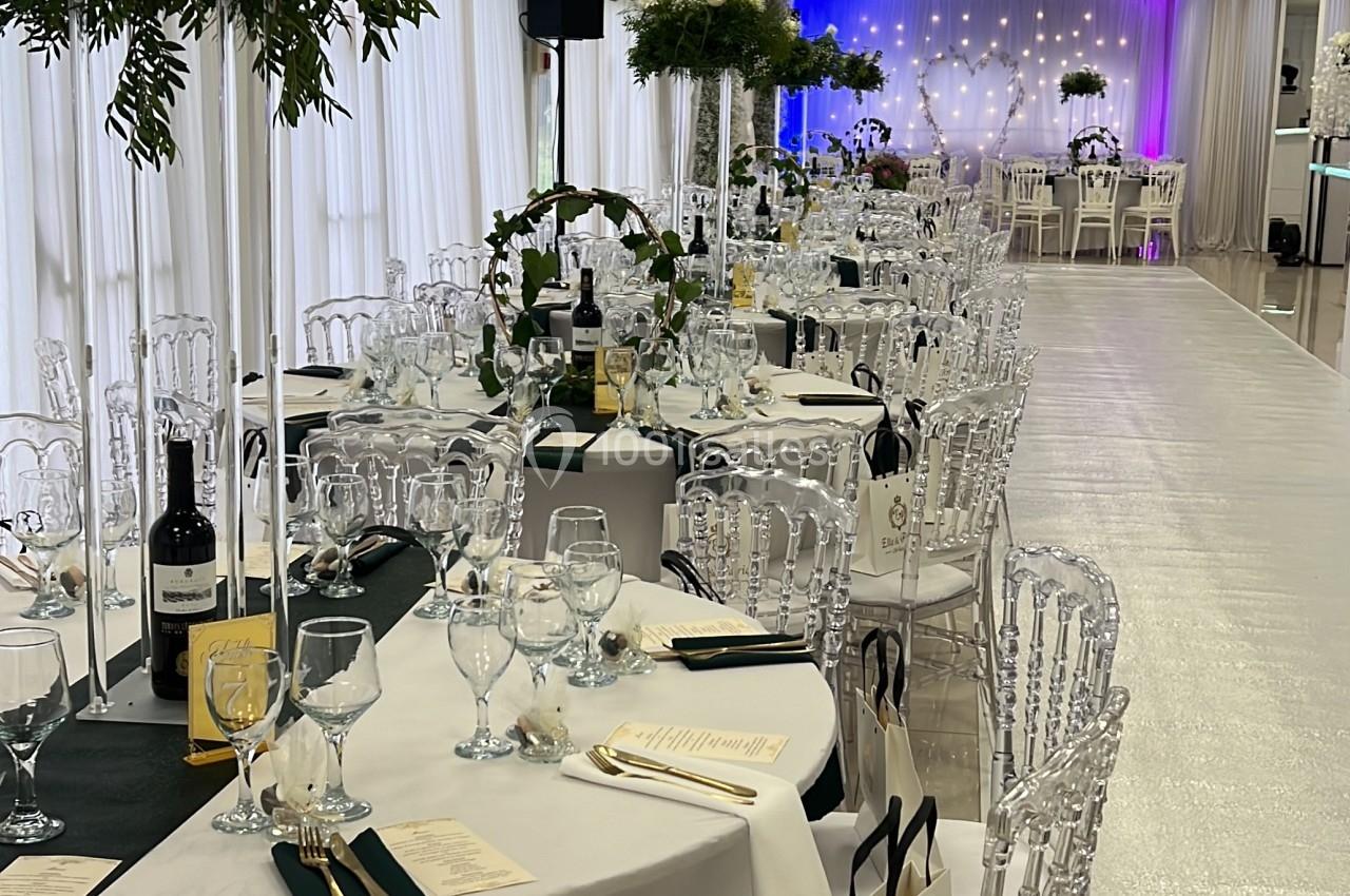 Salle de réception décorée avec des tables dressées, chaises transparentes et éclairage coloré en arrière-plan.