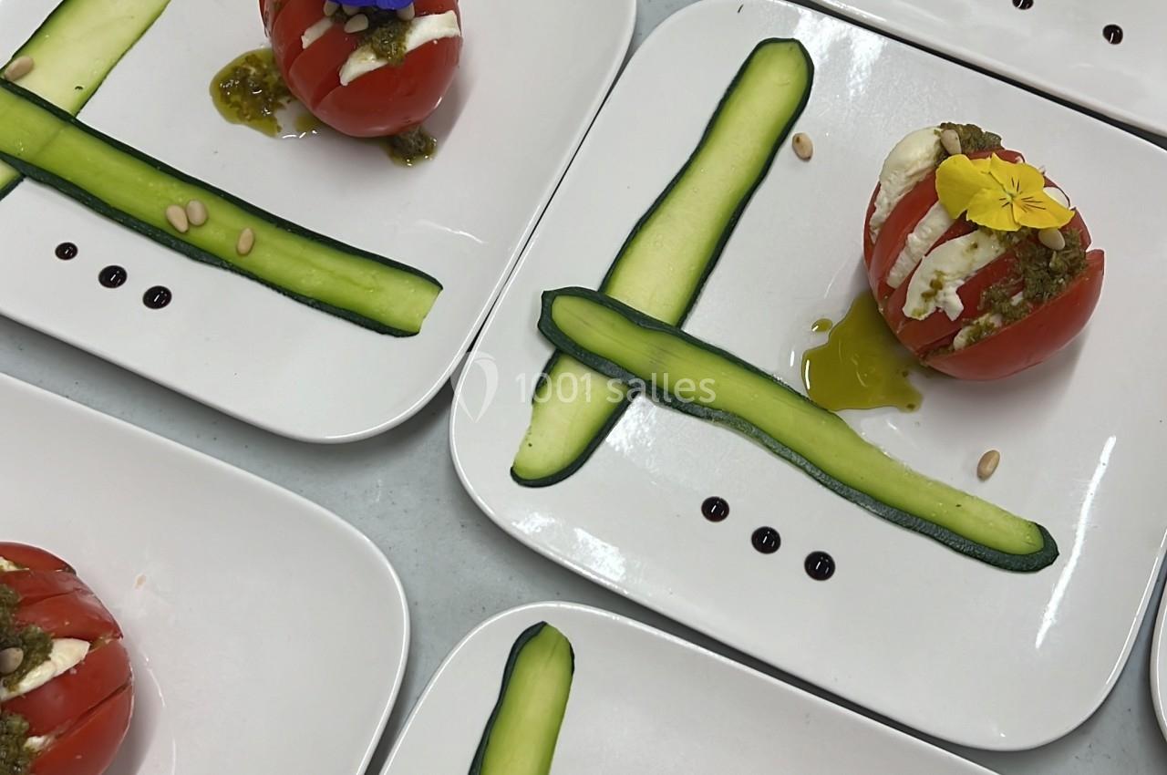 Assiettes avec tomates farcies garnies de fleurs comestibles, accompagnées de tranches de courgettes et de sauce.