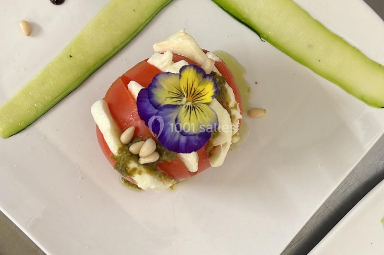 Assiette décorée avec une entrée composée de légumes, fromage, fleur comestible et traits de sauce balsamique.