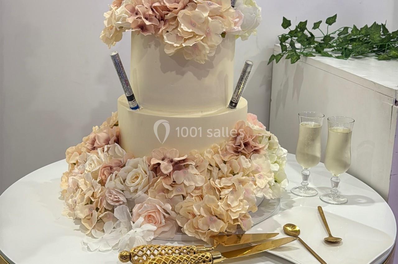 Gâteau de mariage à trois étages décoré de fleurs pastel, posé sur une table ronde avec des couverts dorés.
