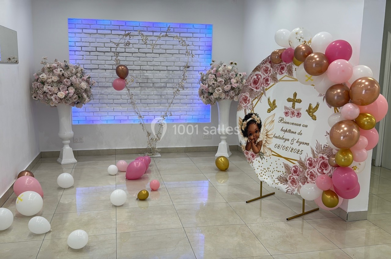 Salle décorée pour une célébration avec ballons, fleurs, panneau personnalisé et éclairage mural en forme de cœur.