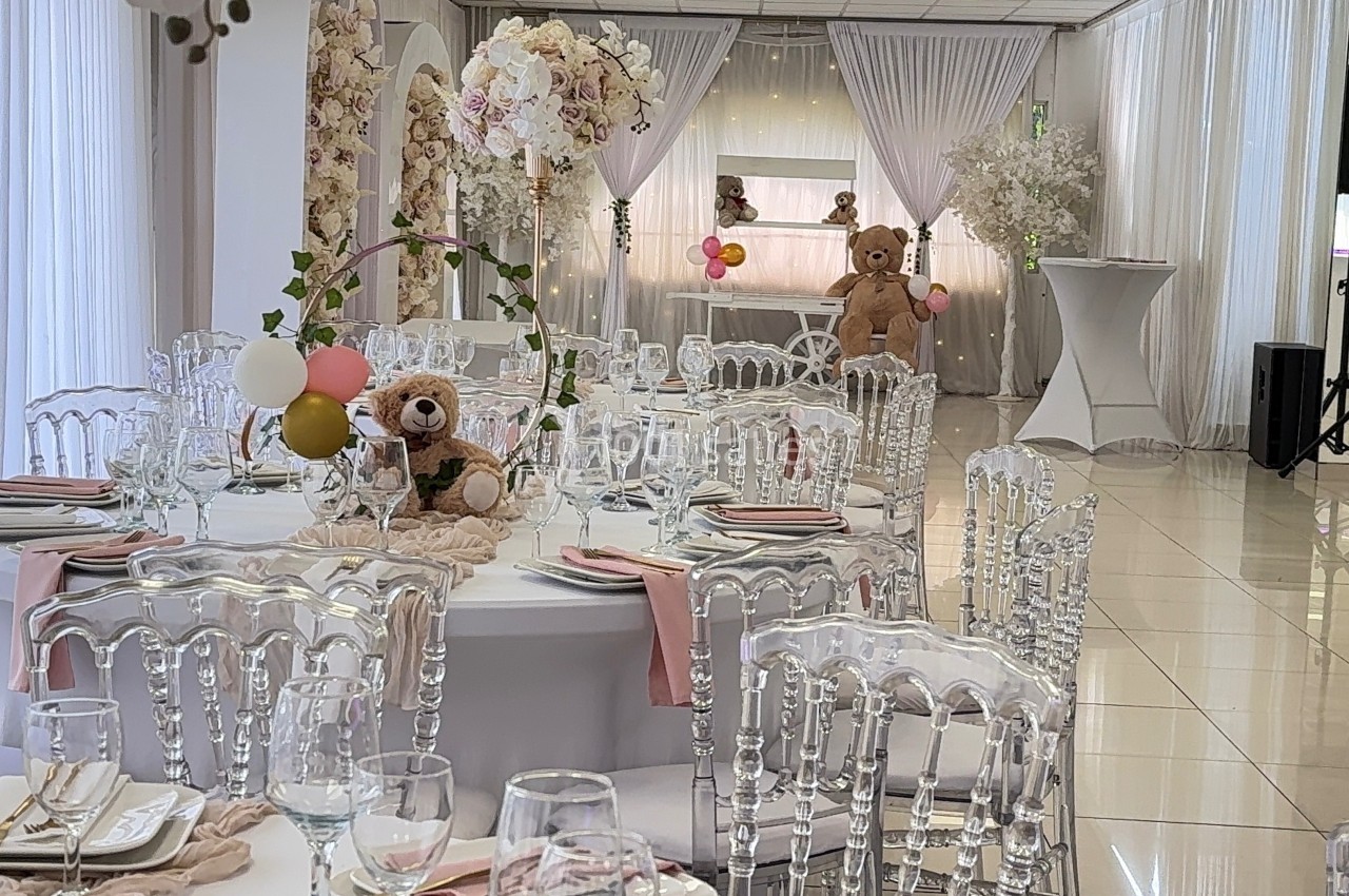 Salle de réception décorée avec des tables rondes, des chaises transparentes et des éléments floraux, ambiance festive.