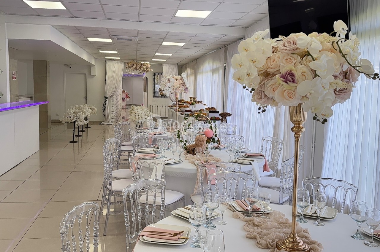 Salle de réception décorée avec des tables élégantes, des chaises transparentes et des centres de table floraux.