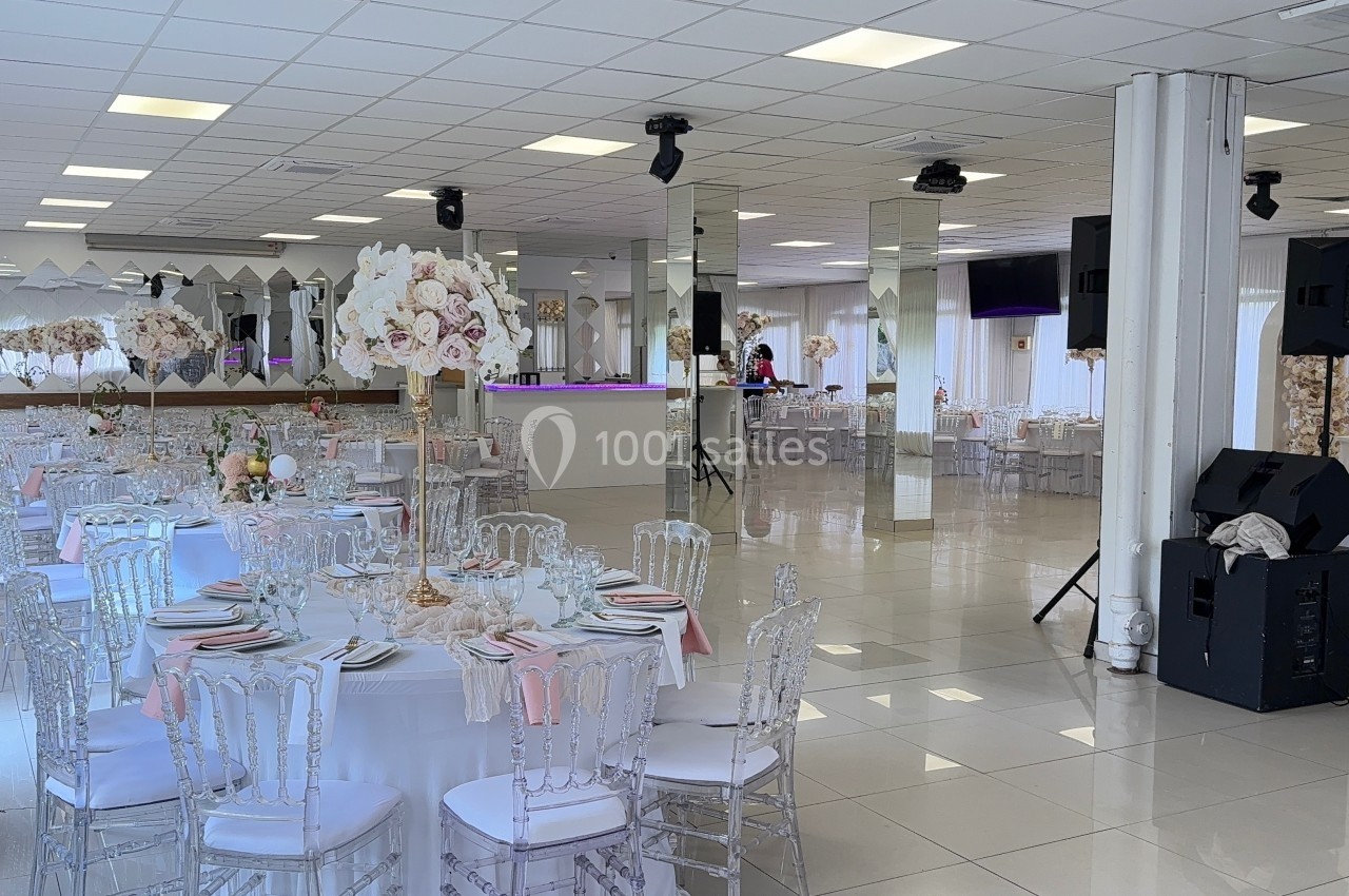 Salle de réception lumineuse avec tables élégamment dressées, chaises transparentes et décorations florales.
