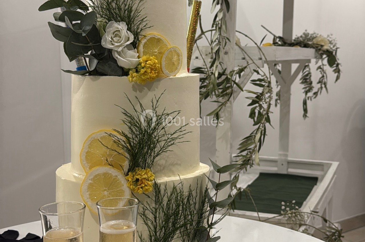 Gâteau de mariage à trois étages décoré de citrons, fleurs jaunes et blanches, avec deux verres de champagne devant.