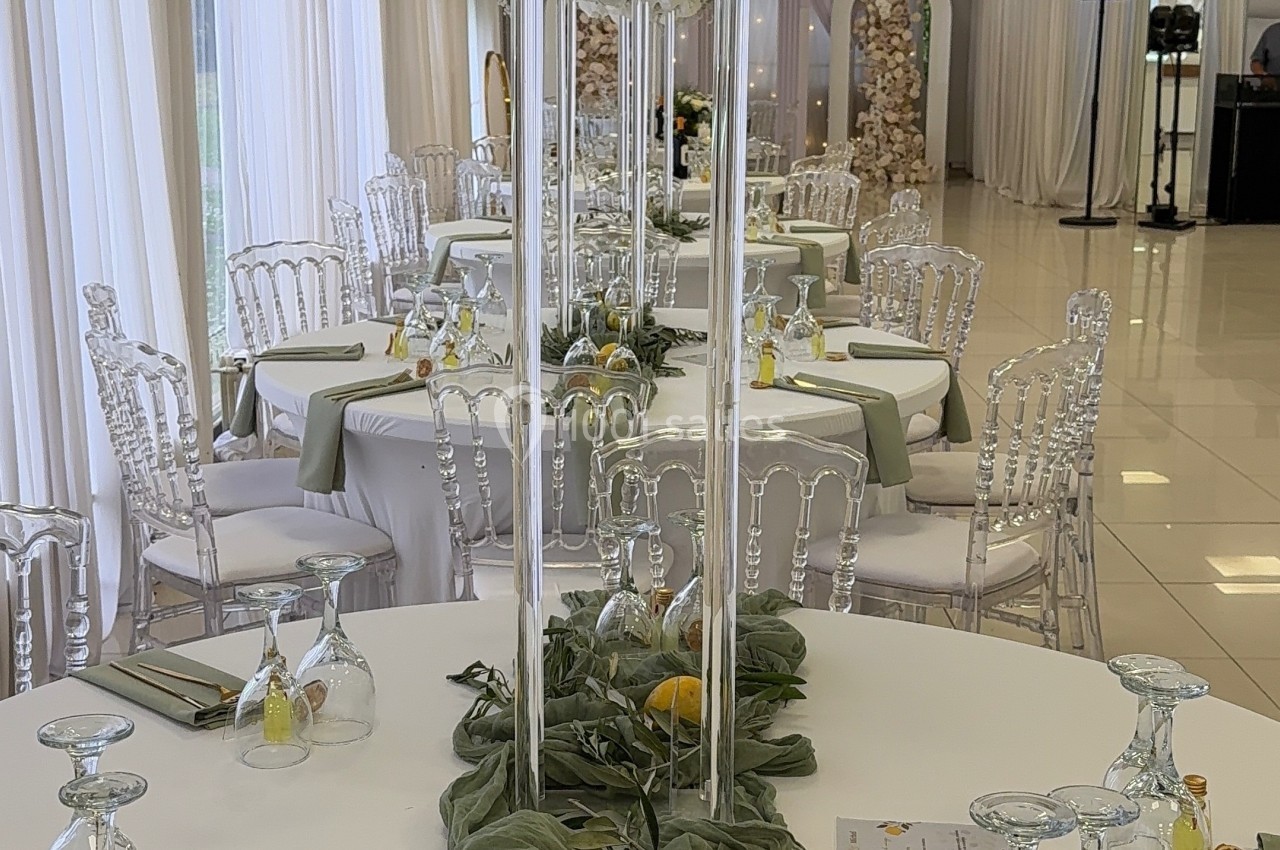 Centre de table avec vase haut, fleurs blanches, citrons et décoration verte sur une table dressée élégamment.