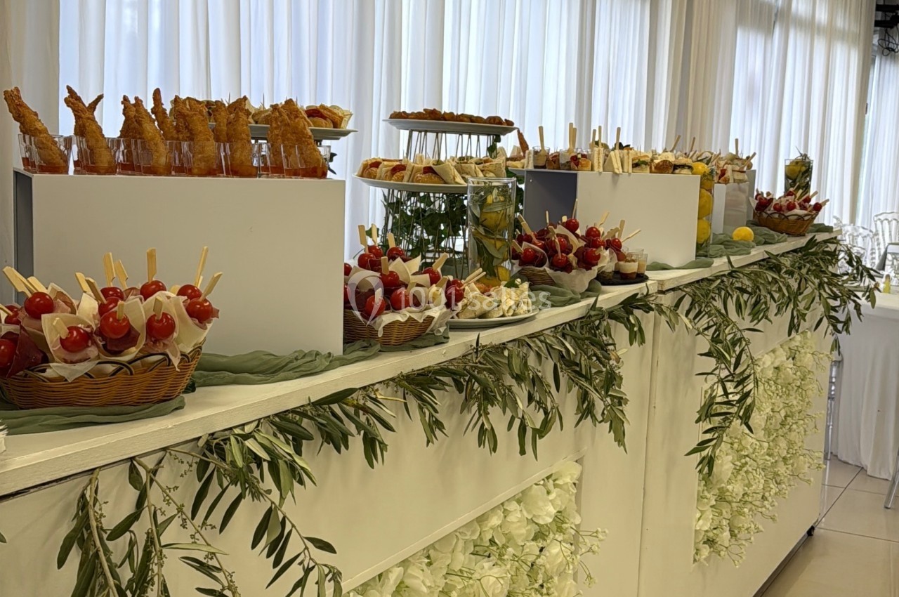 Buffet décoré de fleurs blanches avec des amuse-bouches variés disposés sur des plateaux dans une salle lumineuse.