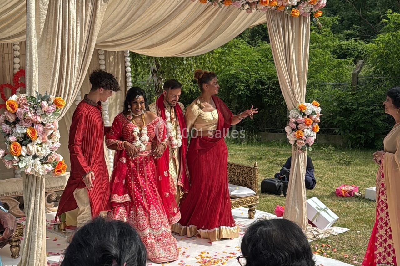 Un mariage en plein air sous une arche décorée de fleurs, avec des personnes en tenues traditionnelles colorées.