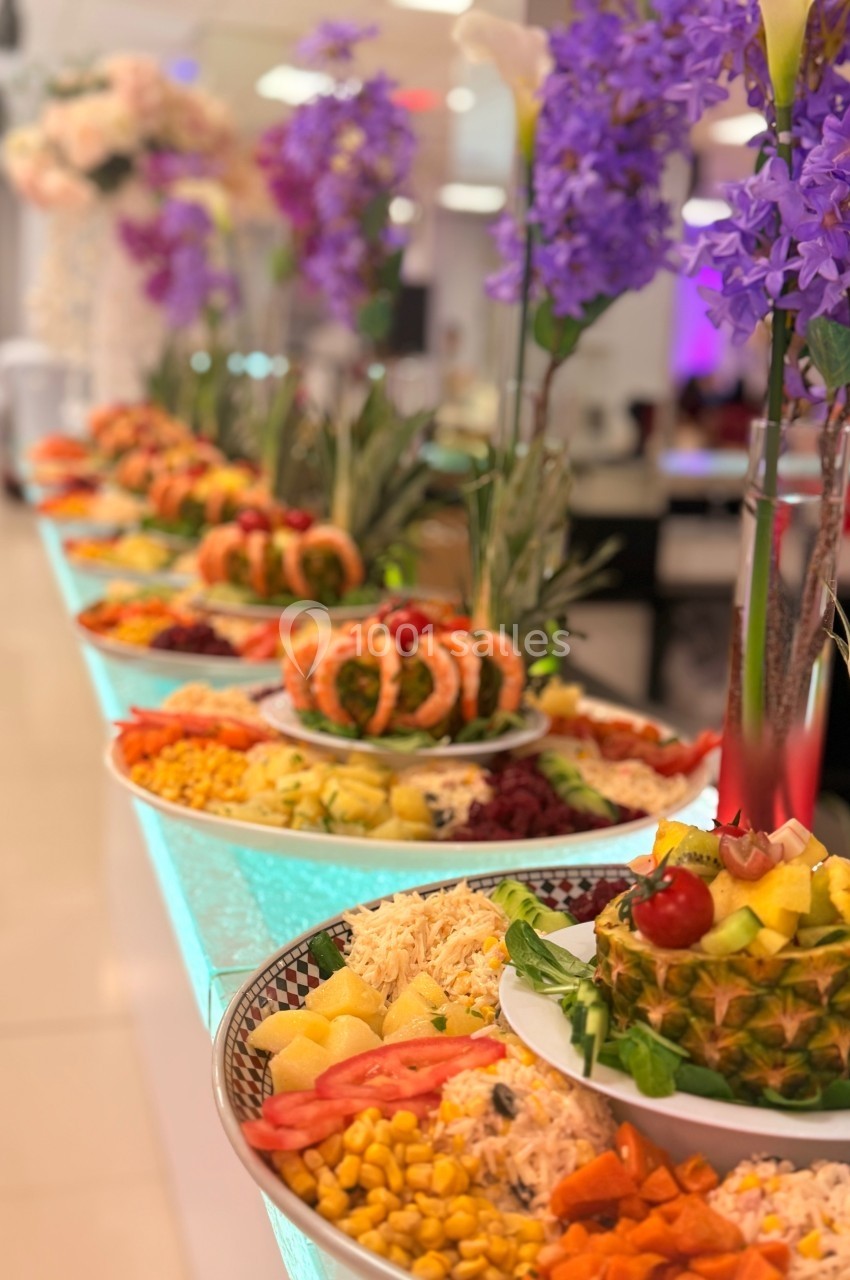 Buffet coloré avec des plats variés, incluant fruits, légumes et décorations florales sur une table lumineuse.