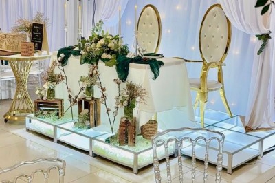 Salle lumineuse avec buffet décoré de fleurs, contenant des plats et boissons, sur un sol en carrelage blanc.