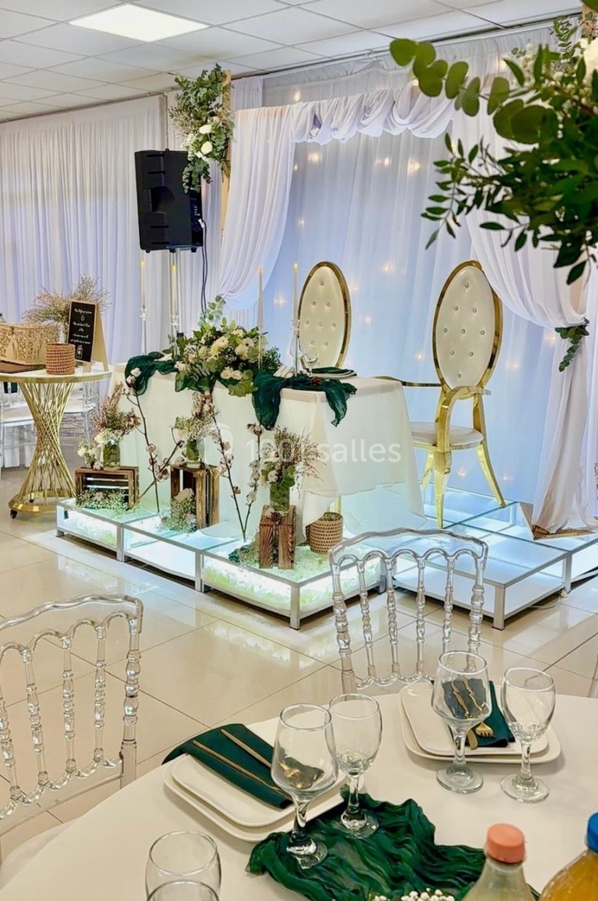 Salle de réception décorée avec des chaises dorées, table d'honneur surélevée et éléments floraux verts et blancs.