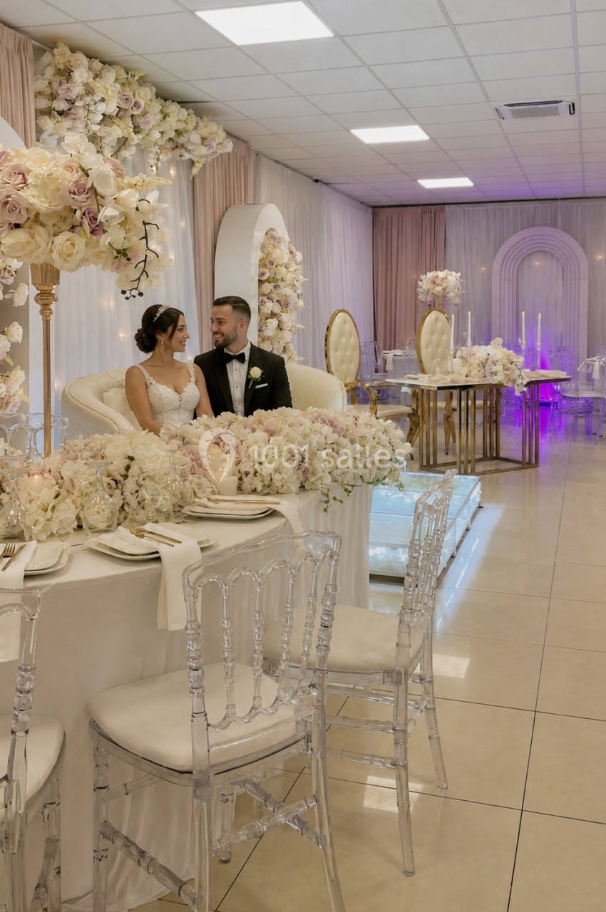 Un couple assis à une table ornée de fleurs dans une salle de réception décorée pour un mariage.