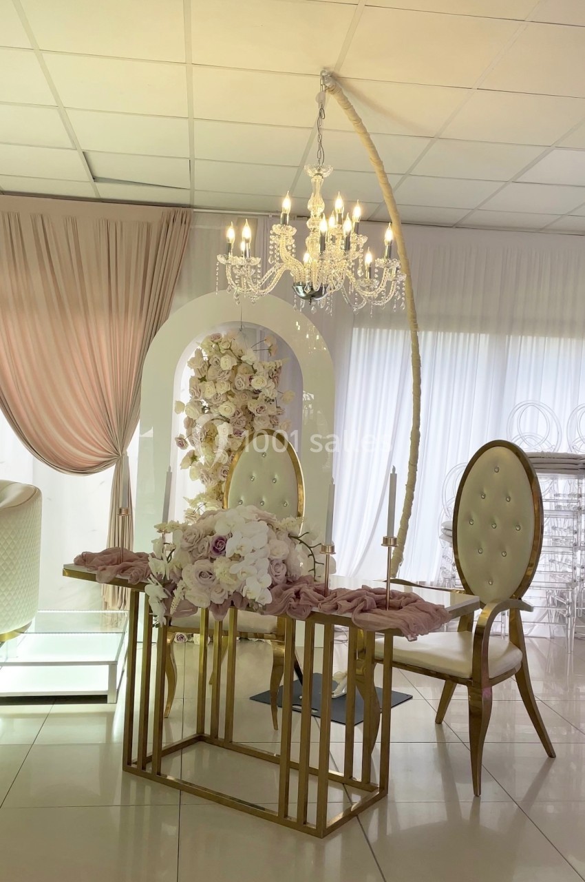 Table décorée avec des fleurs roses et blanches, chaises élégantes et lustre suspendu dans une salle lumineuse.