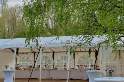 Miniature Location salle Beauchamp (Val-d'Oise) - L'instant Gourmand #50 Tente blanche avec tables hautes décorées de fleurs, installée sur une pelouse entourée d'arbres au printemps.
