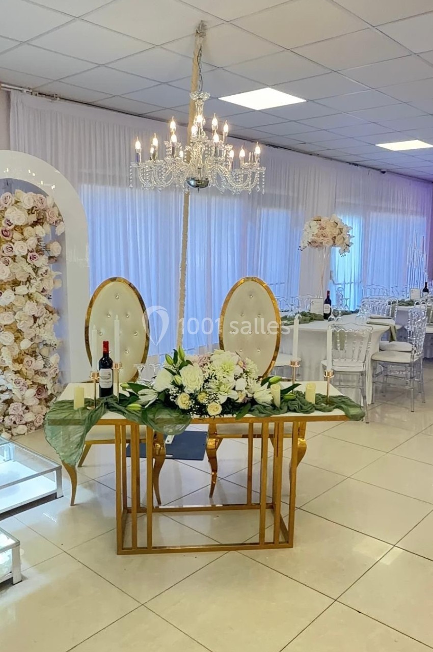 Table décorée avec des fleurs blanches, bougies et bouteilles de vin, entourée de chaises et d'un décor floral élégant.