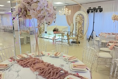 Salle de réception élégante avec tables dressées, chaises transparentes et décoration florale raffinée.