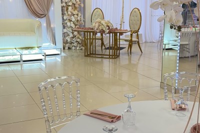 Salle de réception élégante avec tables dressées, chaises transparentes et décoration florale raffinée.