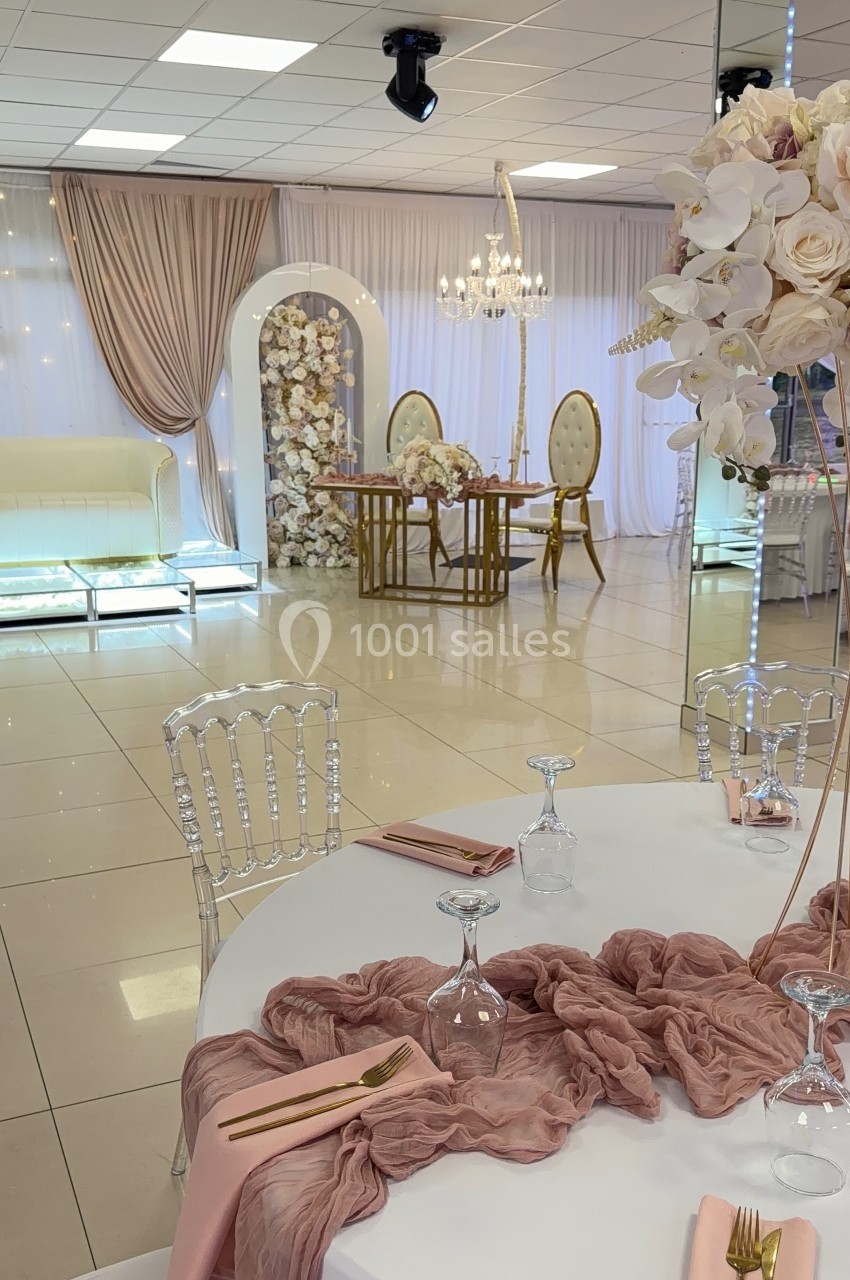 Salle de réception élégante avec table dressée, décoration florale, rideaux roses et mobilier raffiné.