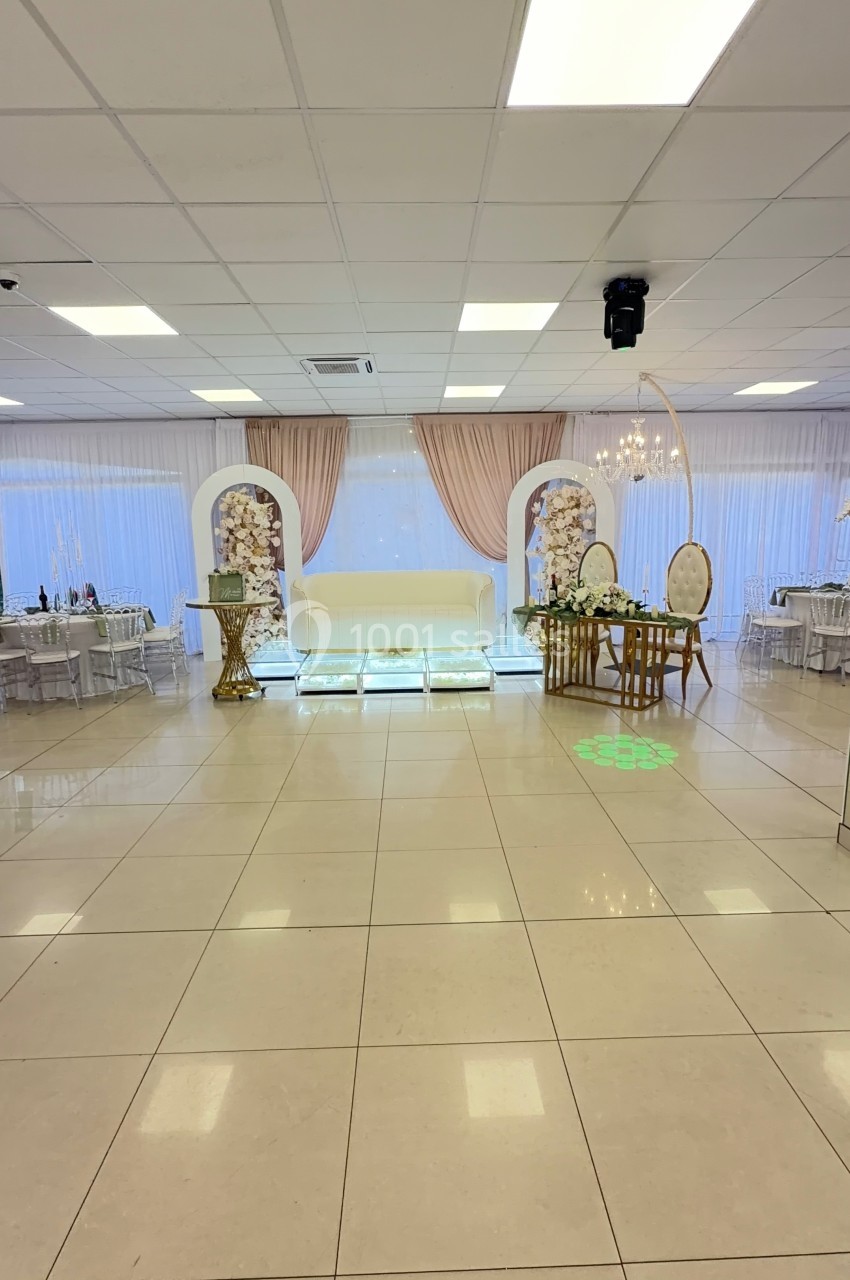 Salle de réception lumineuse avec décor floral, table d'honneur, chaises élégantes et rideaux roses.