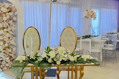 Salle de réception élégante avec tables dressées, chaises transparentes et décoration florale raffinée.
