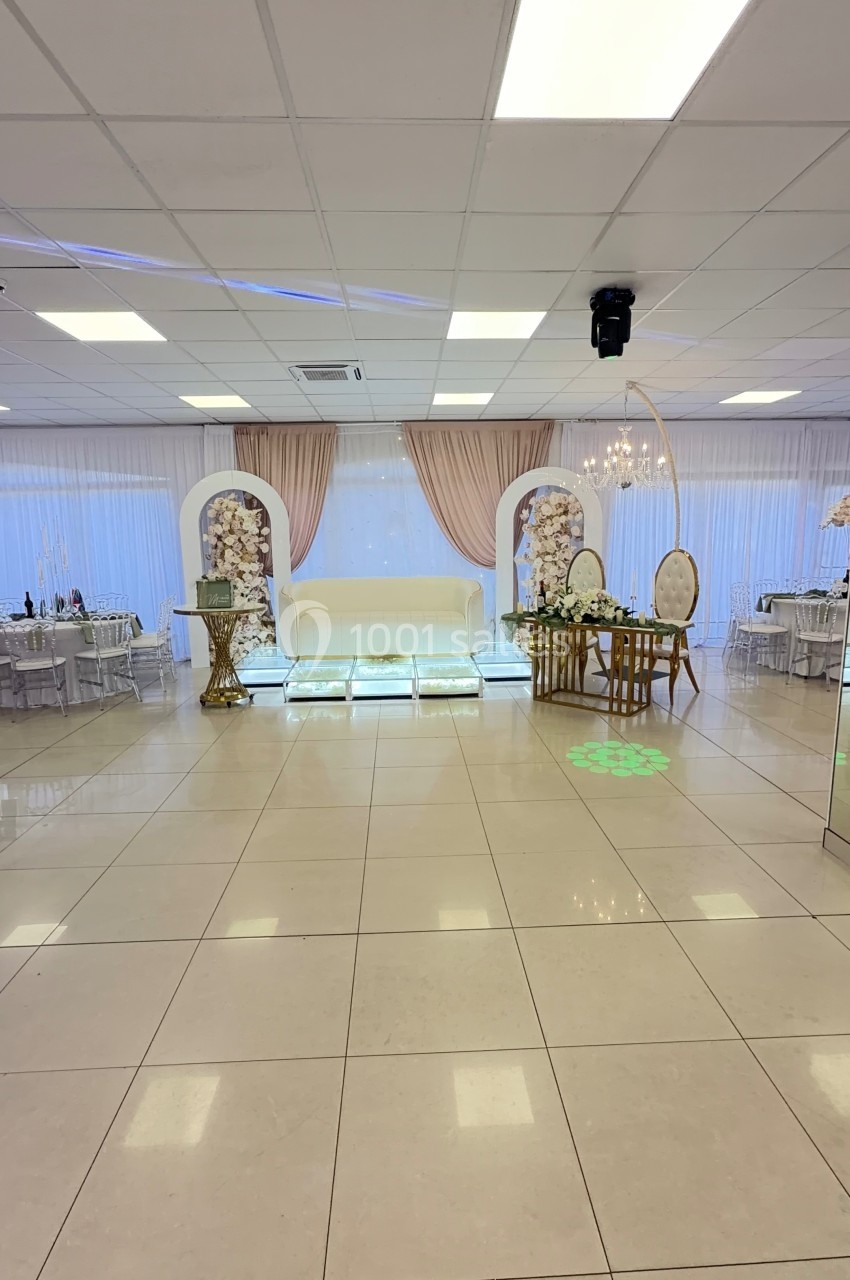 Salle de réception élégante avec canapé blanc, rideaux roses, tables décorées et éclairage lumineux.