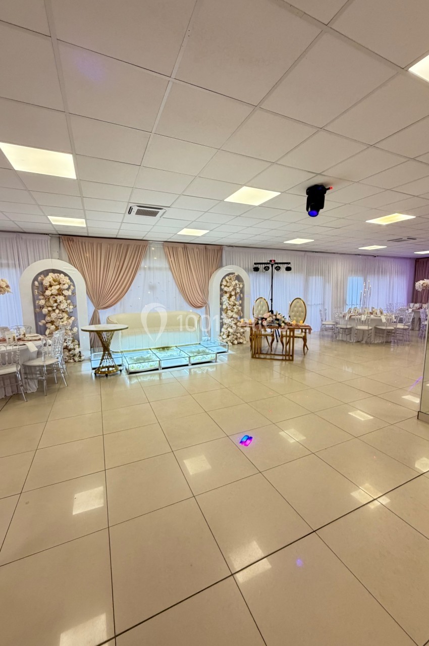 Salle de réception lumineuse avec décorations élégantes, tables dressées et espace central dégagé.