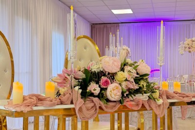 Salle de réception élégante avec tables dressées, chaises transparentes et décoration florale raffinée.