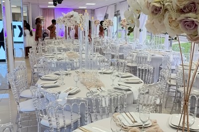 Salle de réception élégante avec tables dressées, chaises transparentes et décoration florale raffinée.