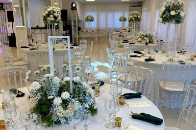 Salle de réception élégante avec tables dressées, chaises transparentes et décoration florale raffinée.