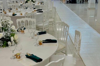 Salle de réception élégante avec tables dressées, chaises transparentes et décoration florale raffinée.