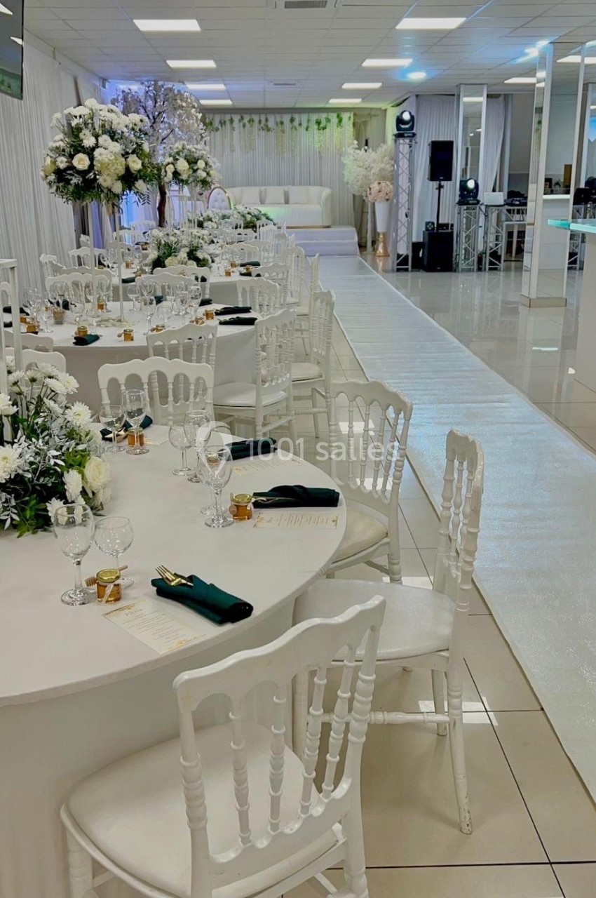 Salle de réception décorée avec des tables rondes, nappes blanches, chaises assorties et arrangements floraux élégants.