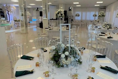 Salle de réception élégante avec tables dressées, chaises transparentes et décoration florale raffinée.