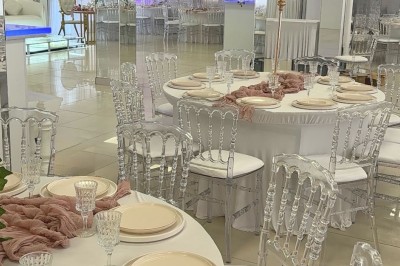 Salle de réception élégante avec tables dressées, chaises transparentes et décoration florale raffinée.