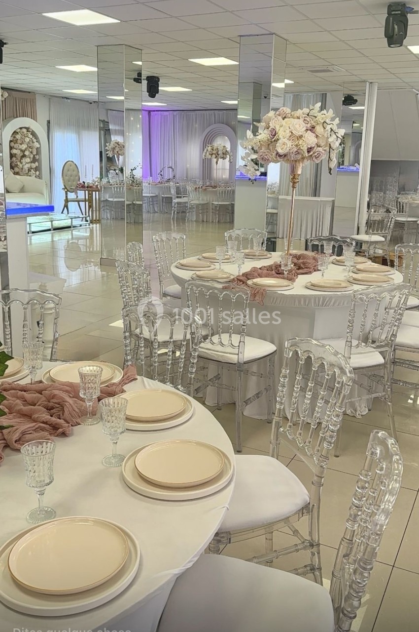 Salle de réception élégante avec tables dressées, chaises transparentes et décoration florale raffinée.