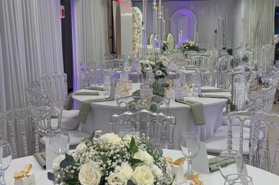 Salle de réception élégante avec tables dressées, chaises transparentes et décoration florale raffinée.
