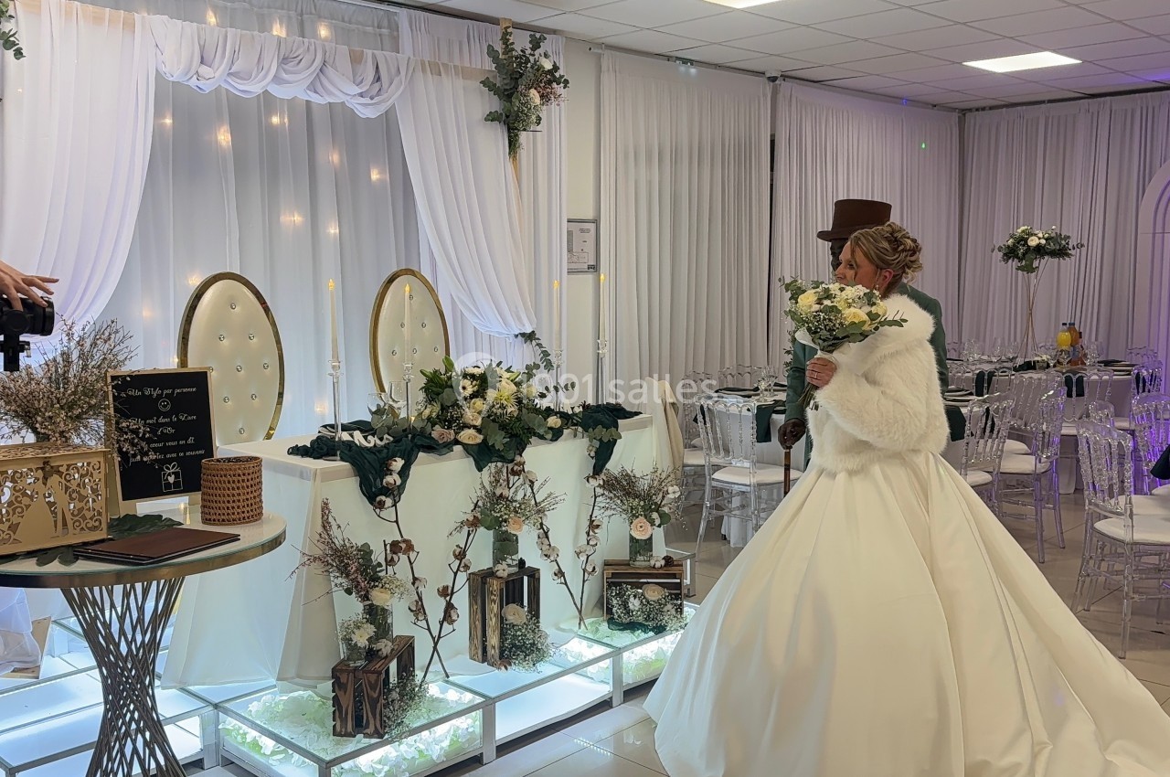 Une mariée en robe blanche tient un bouquet devant une décoration de table de mariage élégante et lumineuse.