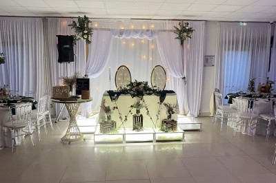 Salle de réception élégante avec tables dressées, chaises transparentes et décoration florale raffinée.