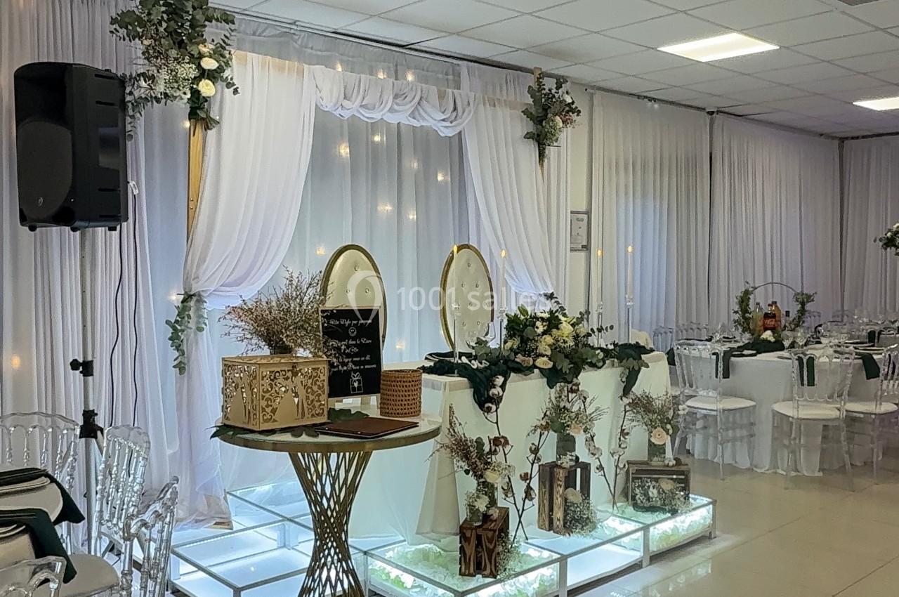 Salle de réception décorée avec des rideaux blancs, des fleurs, des tables dressées et un éclairage chaleureux.