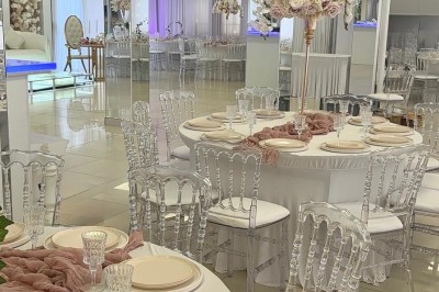 Salle de réception élégante avec tables dressées, chaises transparentes et décoration florale raffinée.