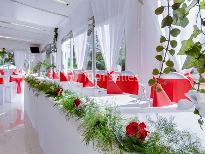 Salle de réception décorée avec des nappes blanches, serviettes rouges et guirlandes de feuillage et fleurs.