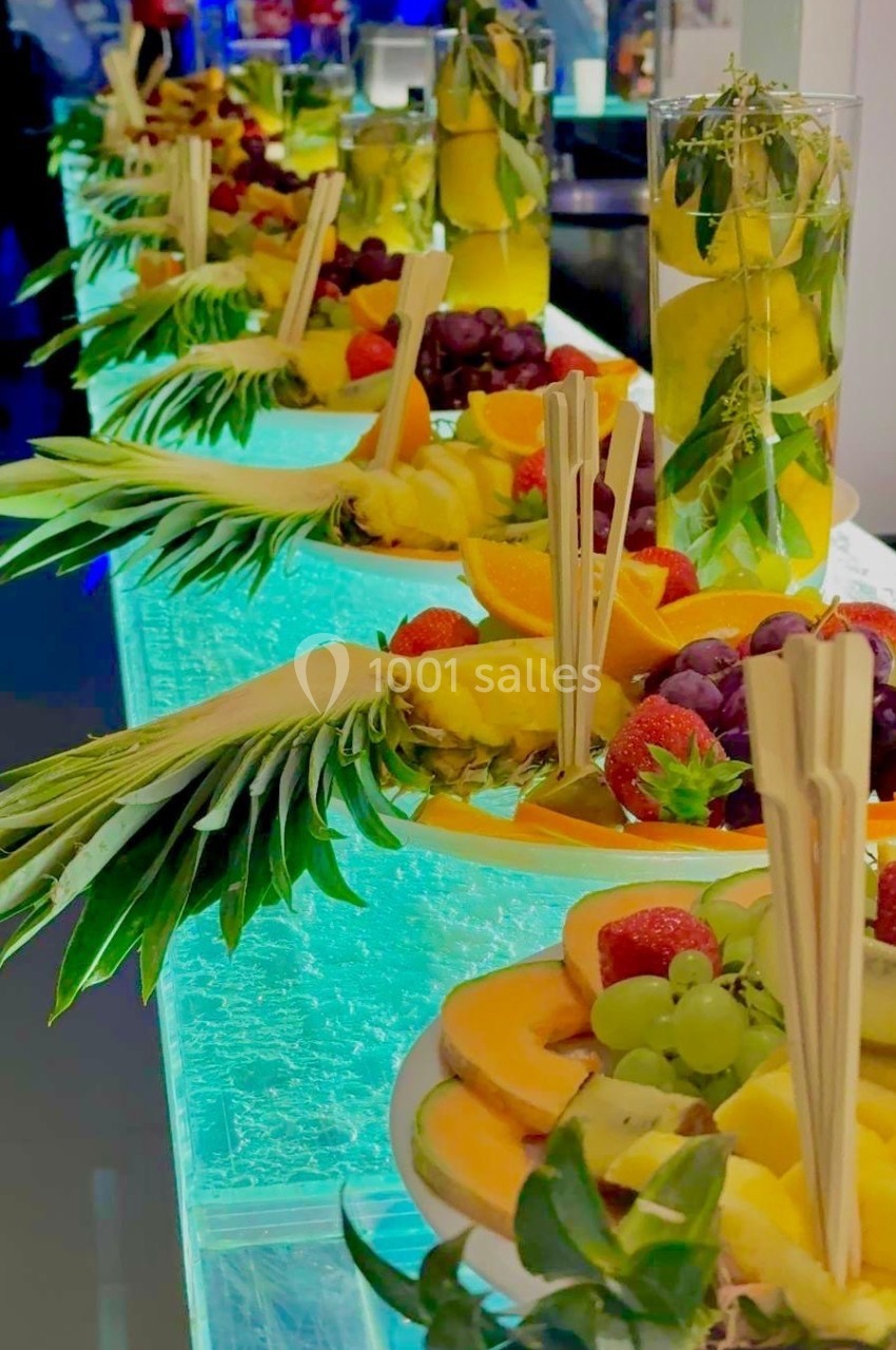 Plateau de fruits frais variés avec ananas, raisins, fraises et oranges, disposés sur une table lumineuse.