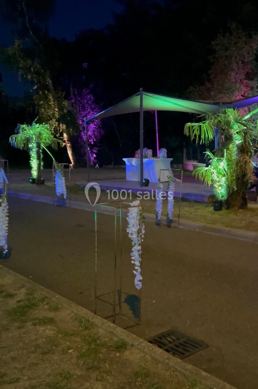 Allée décorée de fleurs blanches et éclairages colorés menant à un espace couvert en extérieur, de nuit.