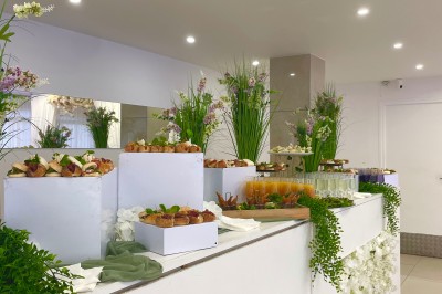 Miniature Location salle Beauchamp (Val-d'Oise) - L'instant Gourmand #23 Buffet décoré de fleurs blanches et vertes, avec des plateaux de fruits et de verrines dans une salle lumineuse.