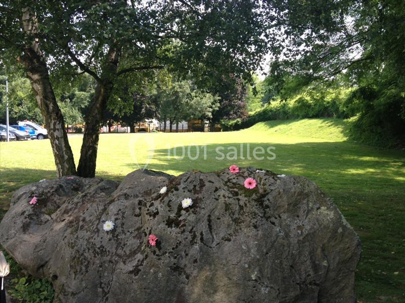 Roc couvert de mousse orné de fleurs colorées, situé dans un parc verdoyant sous des arbres.