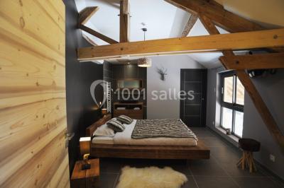 Chambre avec lit rond, couverture rouge, pétales de rose, lampe de chevet et plafond en bois avec suspension plumeuse.
