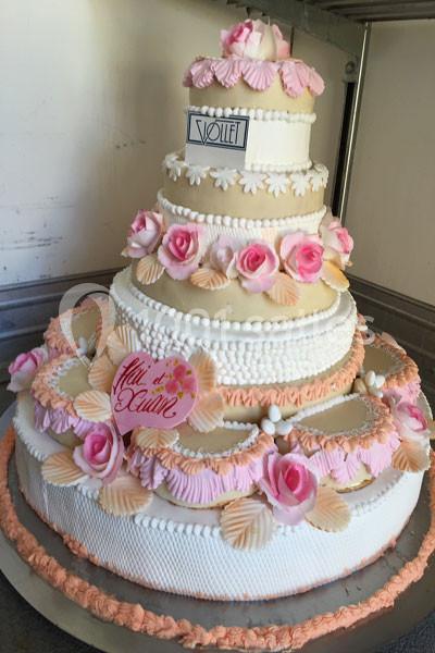 Gâteau de mariage à plusieurs étages décoré de fleurs roses, de perles en sucre et de motifs en crème.