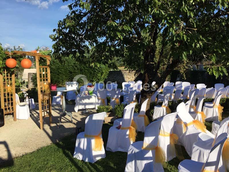 Chaises blanches décorées de rubans orange disposées en extérieur sous un arbre pour une cérémonie.